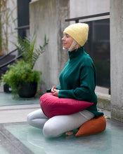Załaduj obraz do przeglądarki galerii, kobieta medytująca na dworze siedząc na pomarańczowej poduszce księżycowej i trzymając drugą poduszkę w kolorze malinowym na nogach