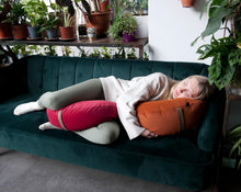 Załaduj obraz do przeglądarki galerii, kobieta która śpi na sofie przytulając poduszkę księżycową w kolorze pomarańczowym i trzymając drugi księżyc malinowy między nogami