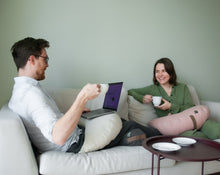 Załaduj obraz do przeglądarki galerii, para pijąca wspólnie kawę na kanapie trzymając na nogach poduszki z gryki w kolorze beżowym i jasno różowym
