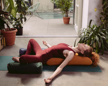 Load image into Gallery viewer, kobieta praktykująca jogę na macie leżąc na żółtej poduszce kopertowej z dwoma małymi wałkami gryczanymi ułożonymi pod kolanami
