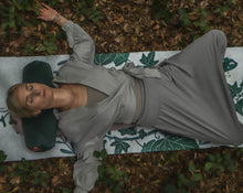 Load image into Gallery viewer, kobieta medytująca w lesie leżąca na macie w liście z zielonym wałkiem gryczanym pod szyją

