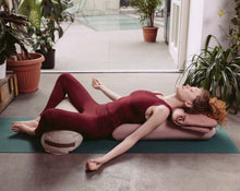 Load image into Gallery viewer, kobieta relaksująca się na macie używając poduszki kopertowej jako podpora pleców i dużego wałka gryczanego jako odciążenie nóg
