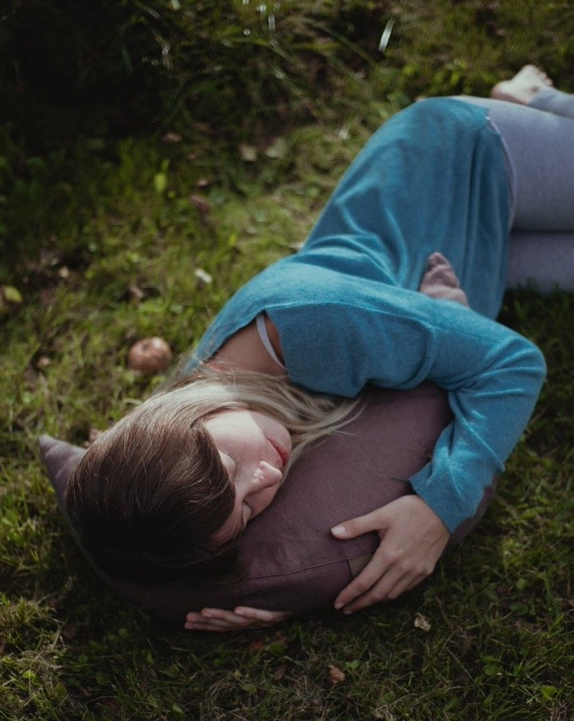 kobieta która śpi na trawie wtulając się w brązową poduszkę księżycową wypełnioną gryką