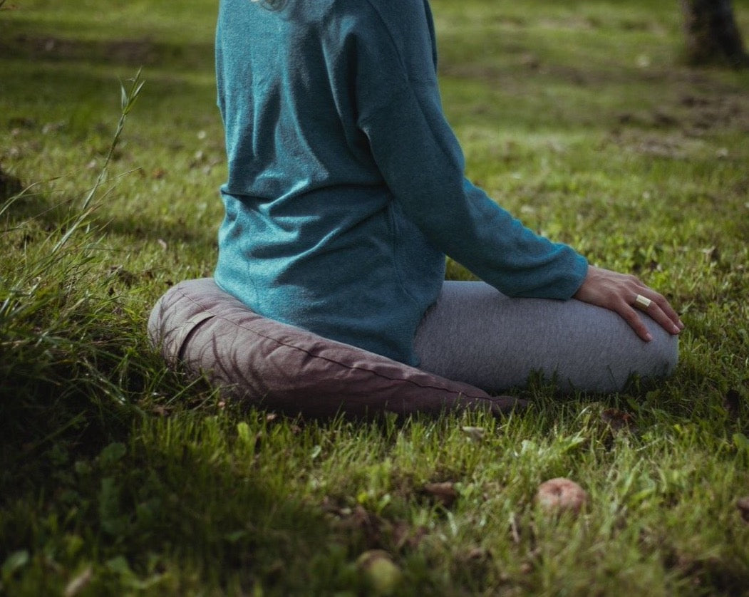 kobieta medytująca na trawie siedząc na brązowej poduszce księżycowej z gryki