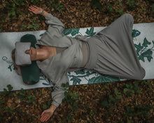 Załaduj obraz do przeglądarki galerii, Kobieta medytująca w lesie leżąc na macie z wałkiem gryczanym pod szyją i poduszką relaksacyjną na oczach
