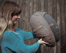Load image into Gallery viewer, kobieta przedstawiająca na tle płotu dwie poduszki księżycowe w kolorze brązowym i grafitowym
