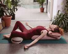Load image into Gallery viewer, Kobieta praktykująca jogę leżąca na poduszce kopertowej z bolsterem gryczanym ułożonym pod kolanami
