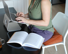 Załaduj obraz do przeglądarki galerii, kobieca pracująca przy laptopie siedząc na białym krześle z pomarańczową poduszką klinową
