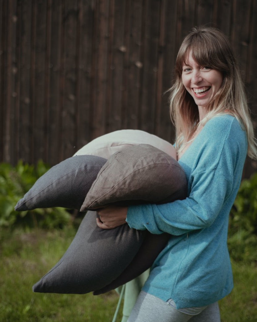 kobieta z uśmiechem idąca i trzymająca w ręce trzy poduszki księżycowe w kolorze jasno beżowym grafitowym i brązowym
